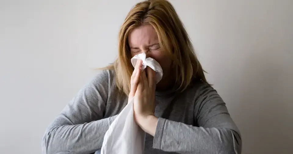 A lady is blowing her nose as she fights allergies and the flu