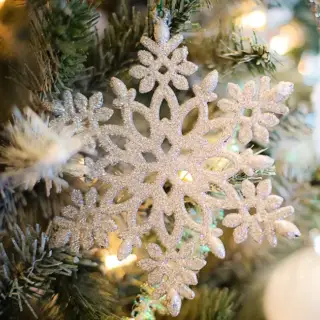 A closeup of a snowflake Christmas ornament on a tree, with dazzling lights behind.