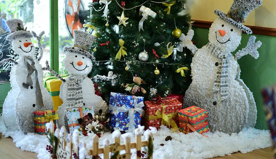 A family of snowmen decorate a living room next to a Christmas tree.