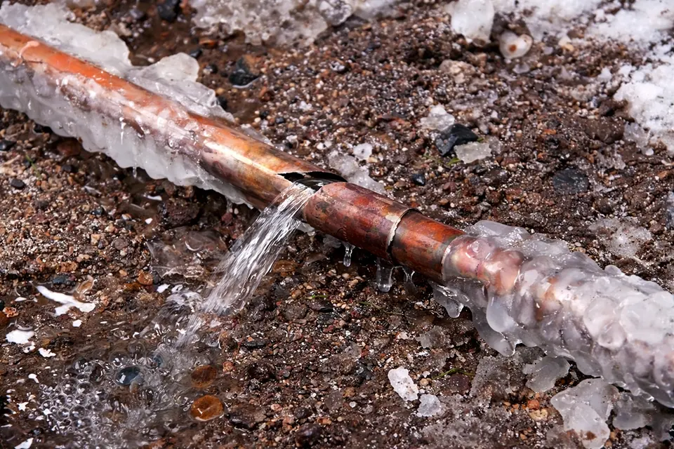 A frozen pipe that has burst, with water spraying out.